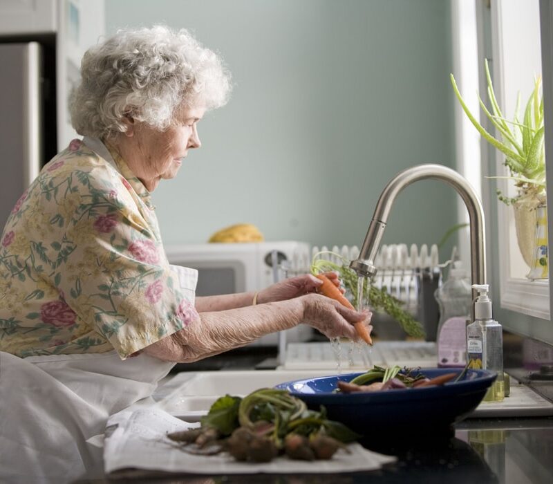 Femme senior dans sa cuisine entrain de laver ses légumes