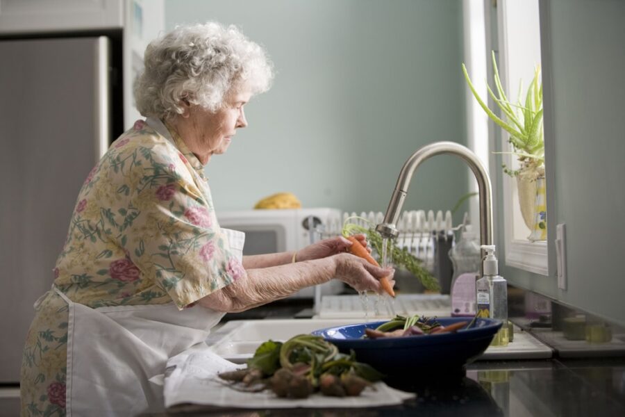 Femme senior dans sa cuisine entrain de laver ses légumes