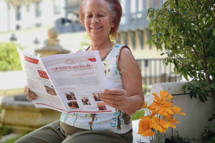 Femme senior assis sur un muret entrain de lire une revue avec un bouquet de fleur à côté d'elle