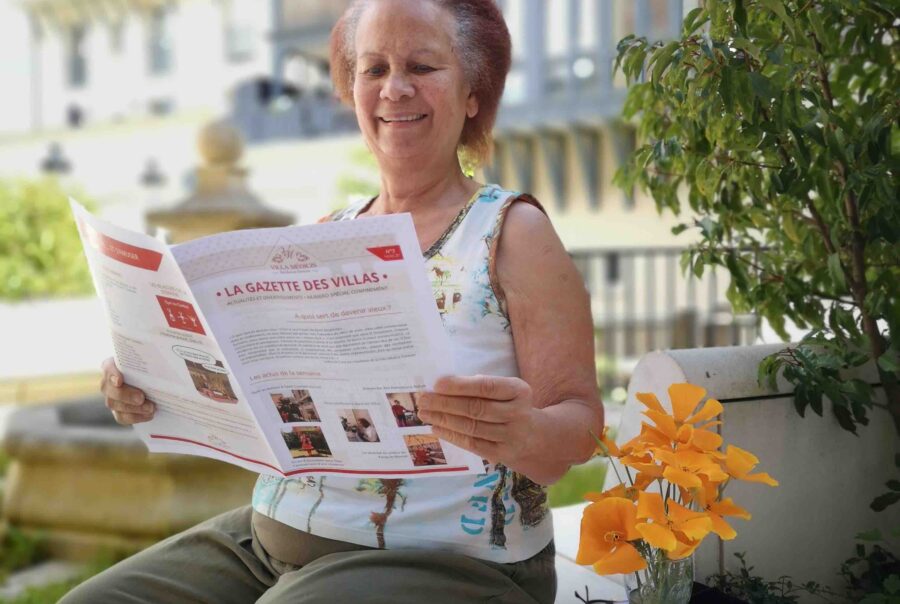 Femme senior assis sur un muret entrain de lire une revue avec un bouquet de fleur à côté d'elle