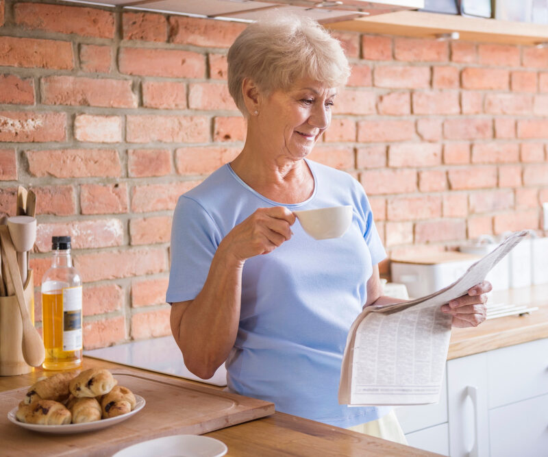 Femme dans sa cuisine prenant un café et regardant un magazine pour senior