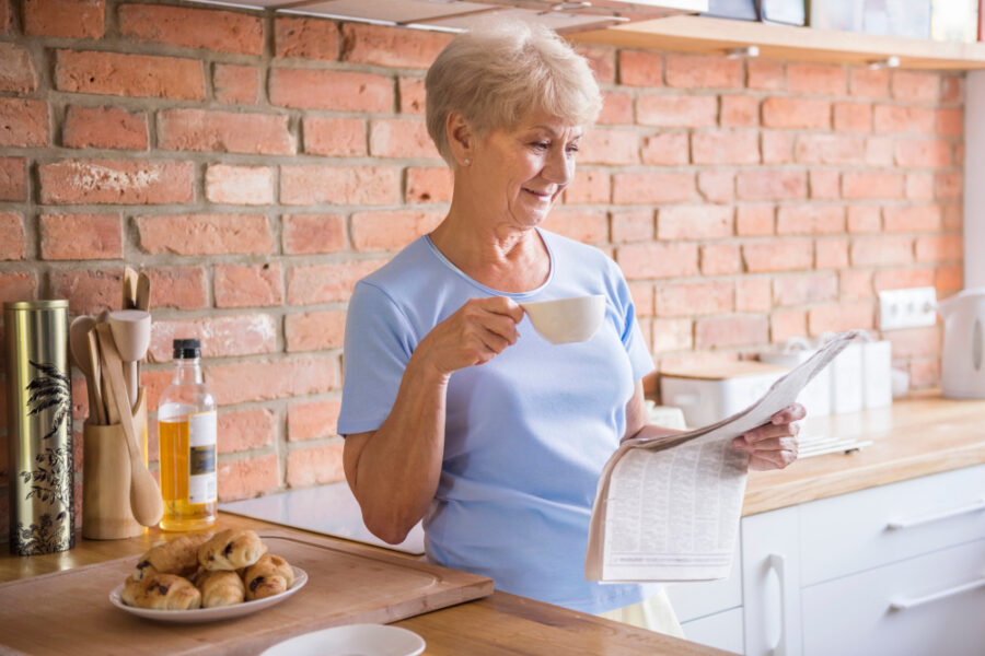 Femme dans sa cuisine prenant un café et regardant un magazine pour senior