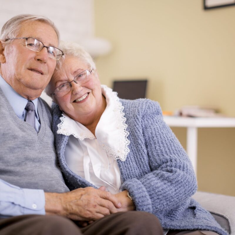 Image d'un couple senior assis sur le canapé qui se tient la main et qui se fait une accolade