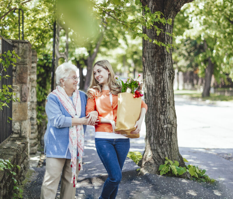 Femme senior marchant dans la rue accompagné d'une aidante qui porte ses courses