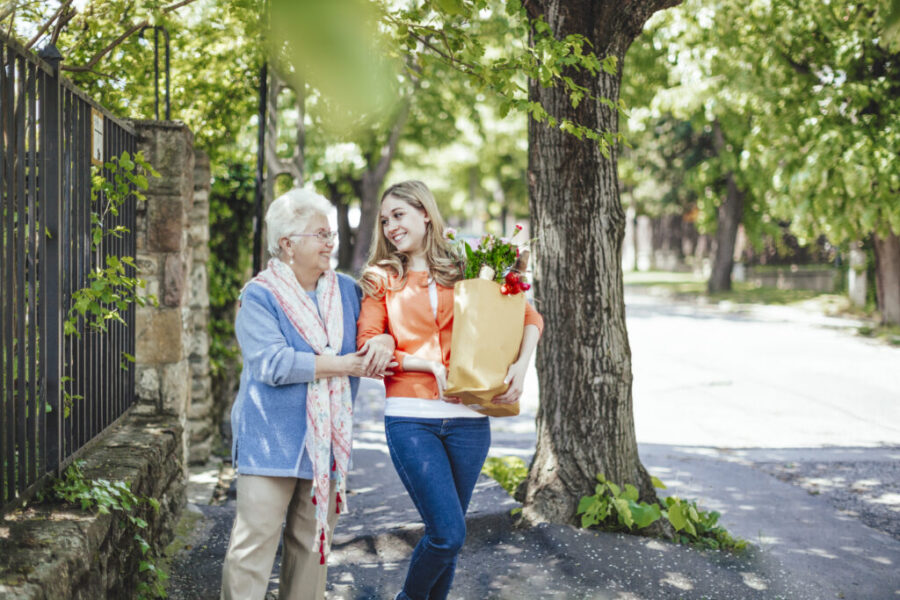 Femme senior marchant dans la rue accompagné d'une aidante qui porte ses courses