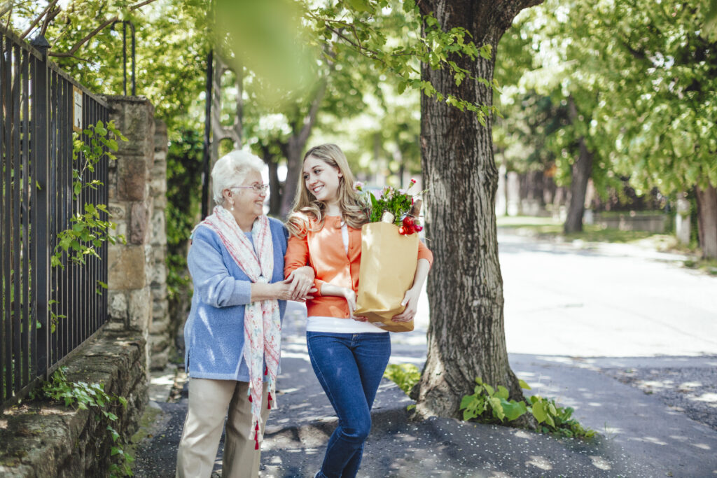 Femme senior marchant dans la rue accompagné d'une aidante qui porte ses courses