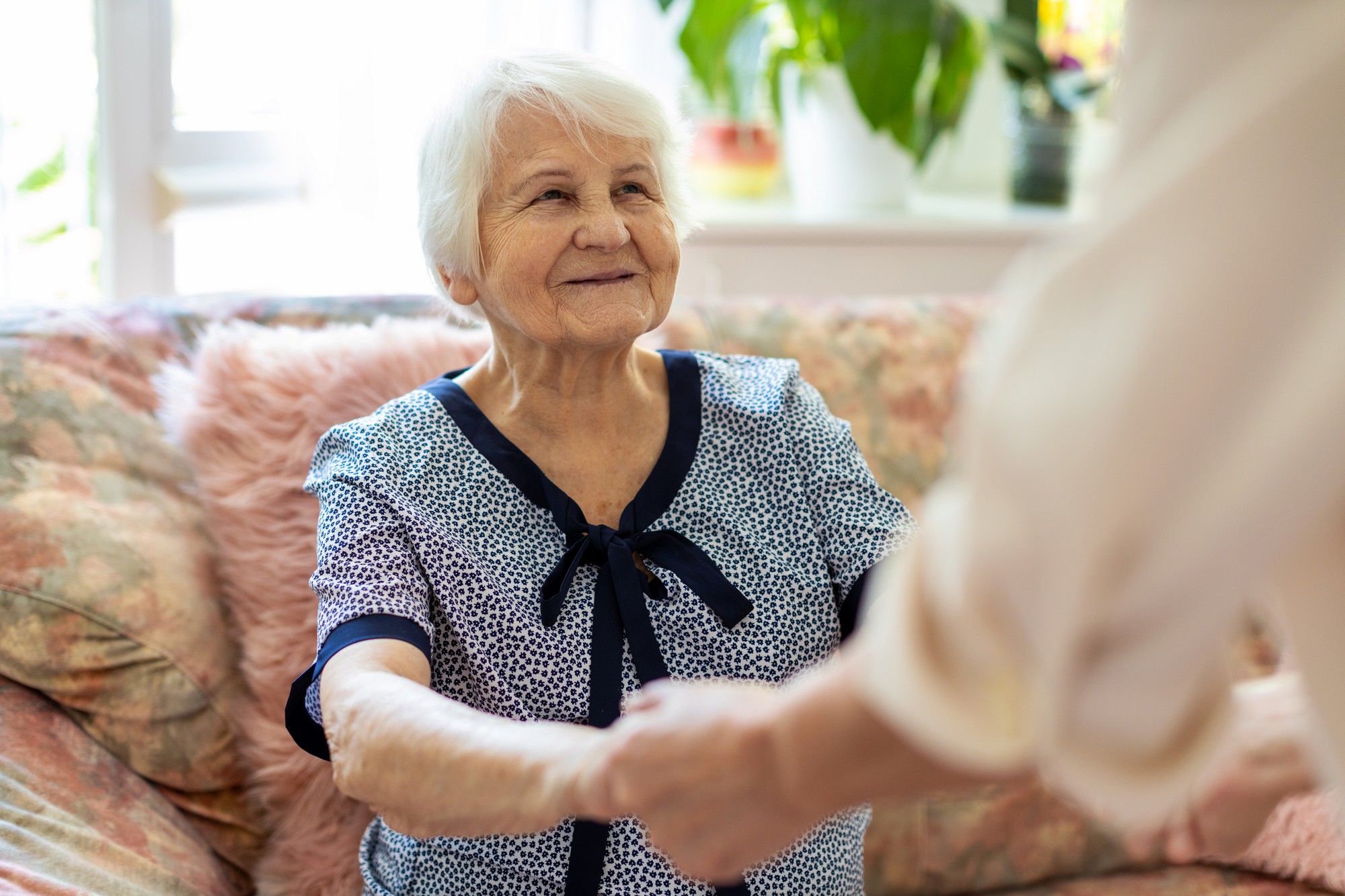 Femme senior assise dans un canapé avec une aidante qui lui tient les mains