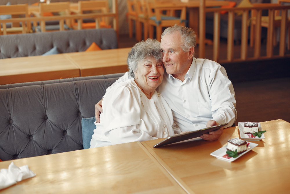 Couple senior en sécurité l'un contre l'autre regardant la tablette et mangeant un dessert