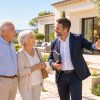 Un couple senior discute avec un agent immobilier devant une villa